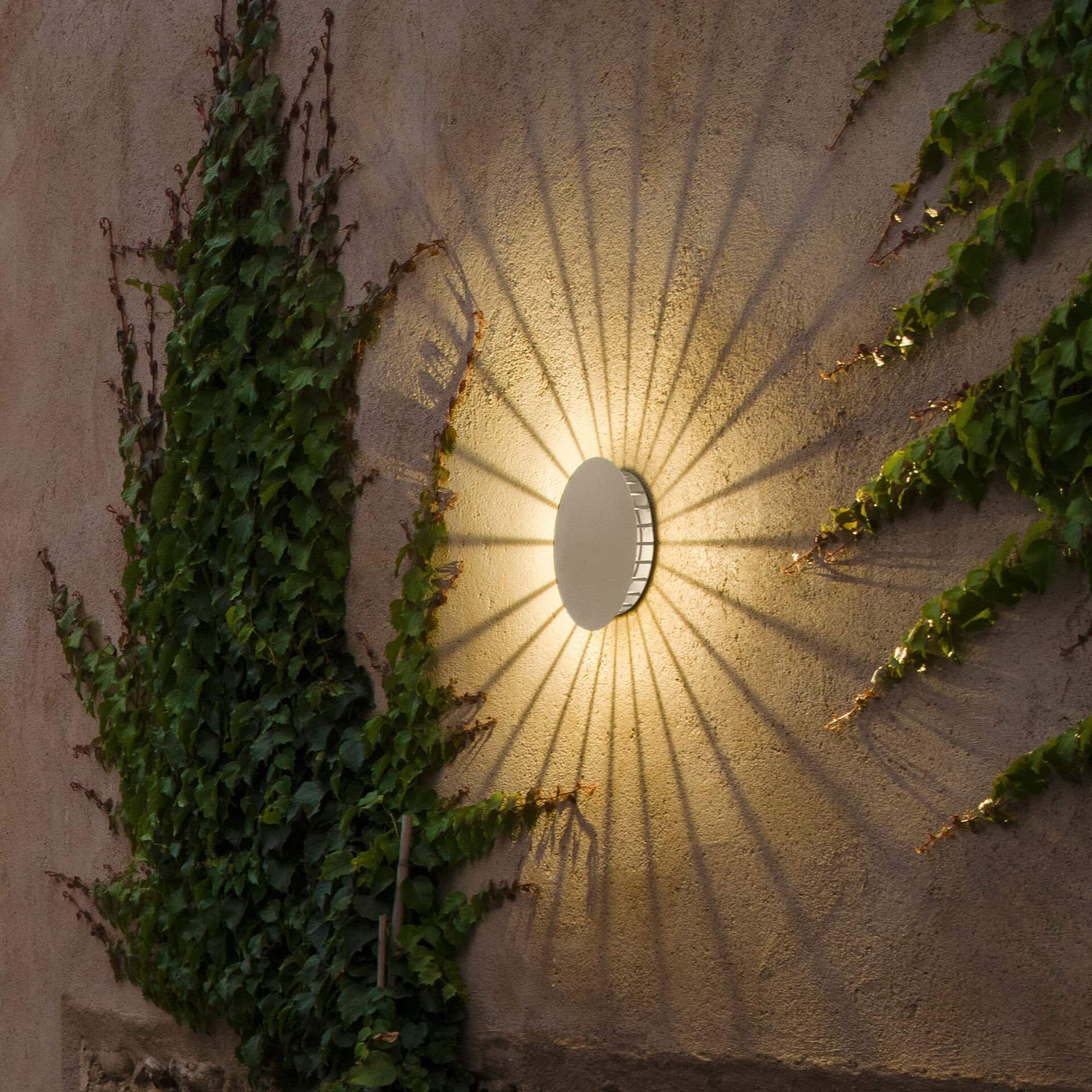 outdoor garden wall with a wall light creating elegant shadows at night, French-inspired lighting design