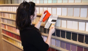 An interior color consultant comparing an orange fabric swatch with paint chips on a studio display wall.