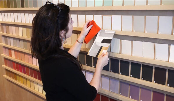 An interior color consultant comparing an orange fabric swatch with paint chips on a studio display wall.
