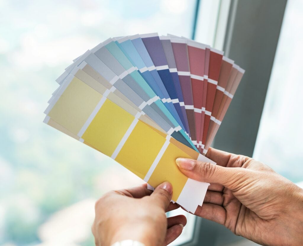 An interior decorator or aspiring designer evaluating paint samples by a window to understand natural light shifts and color undertones.